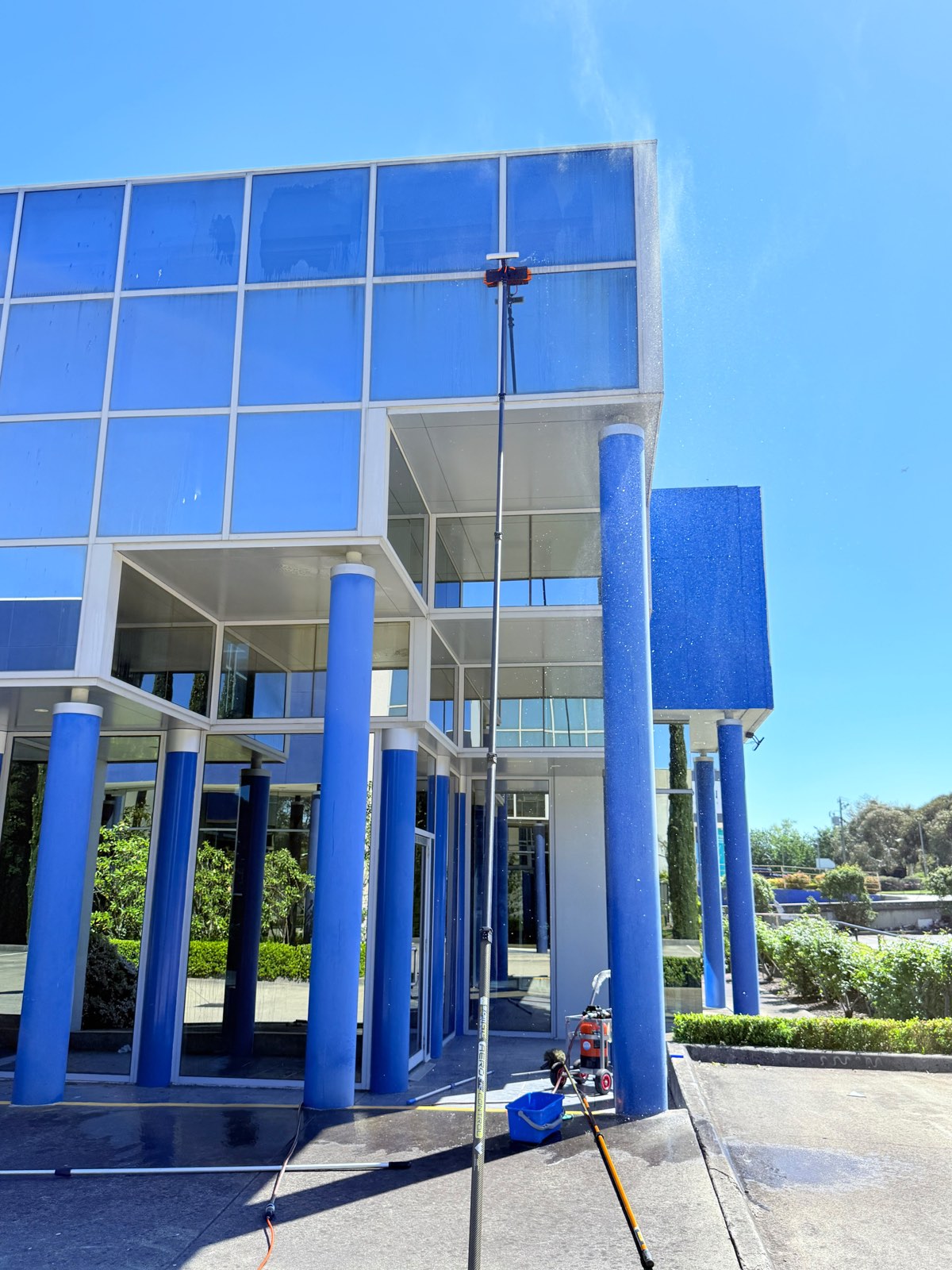 Blue-clad commercial building facade and columns being pressure washed