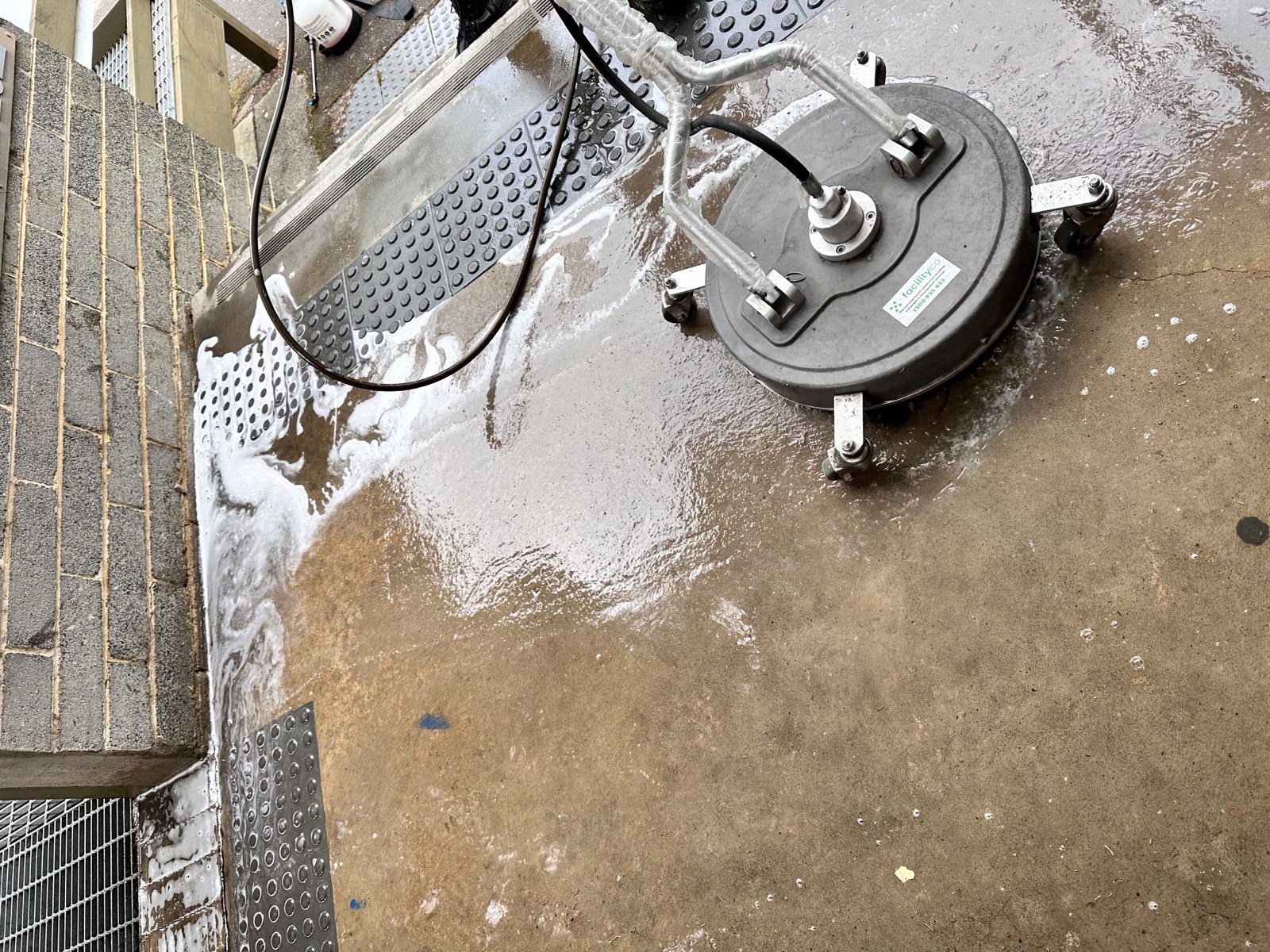 Heavy foam from a pressure washing surface cleaner covering a brick building's front entrance paving