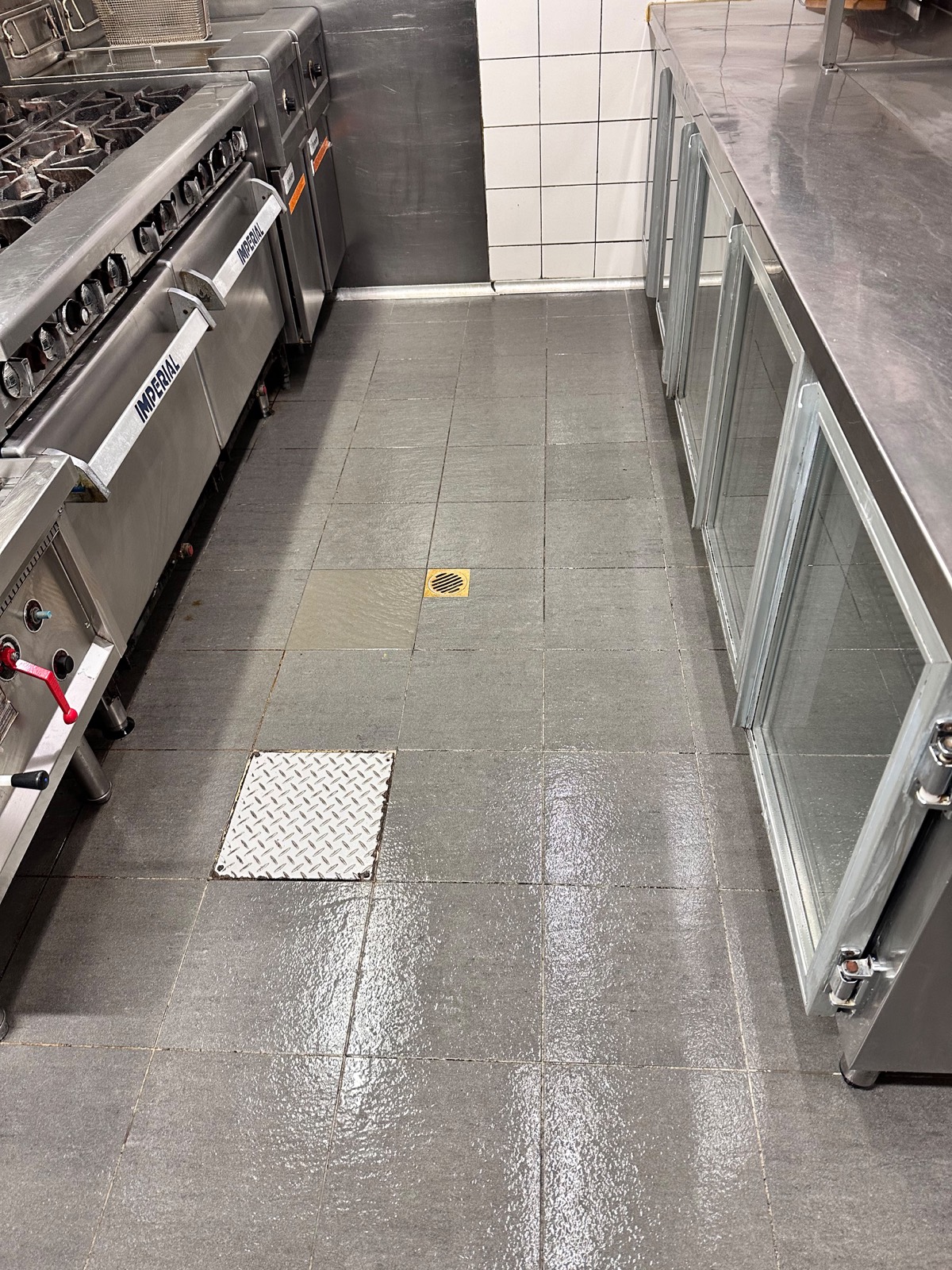 Commercial kitchen tiled floor cleaned around cooking equipment, coolroom doors and floor drain