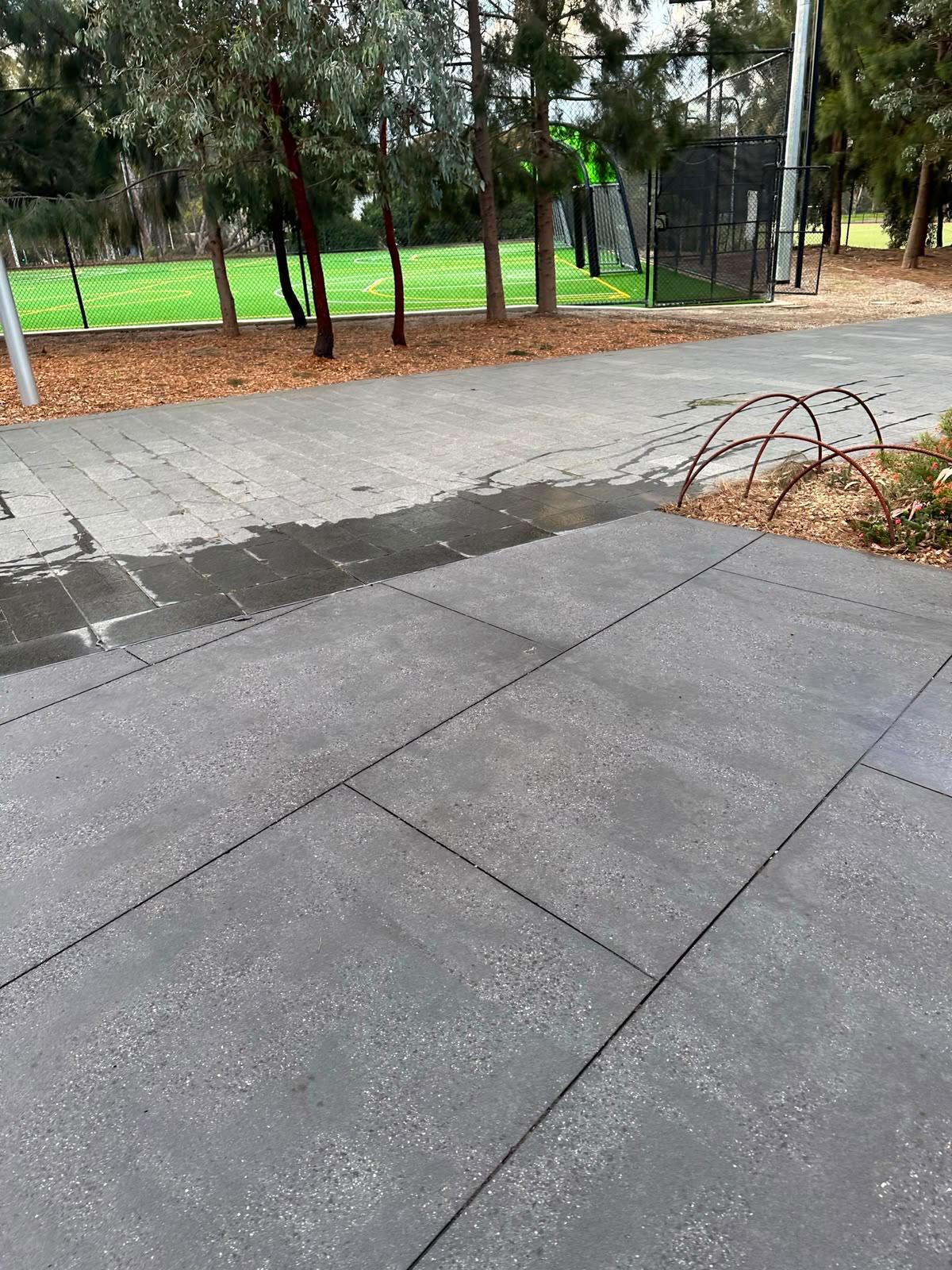 Surface cleaner disc pressure washing a paved courtyard beside a corten steel garden bed
