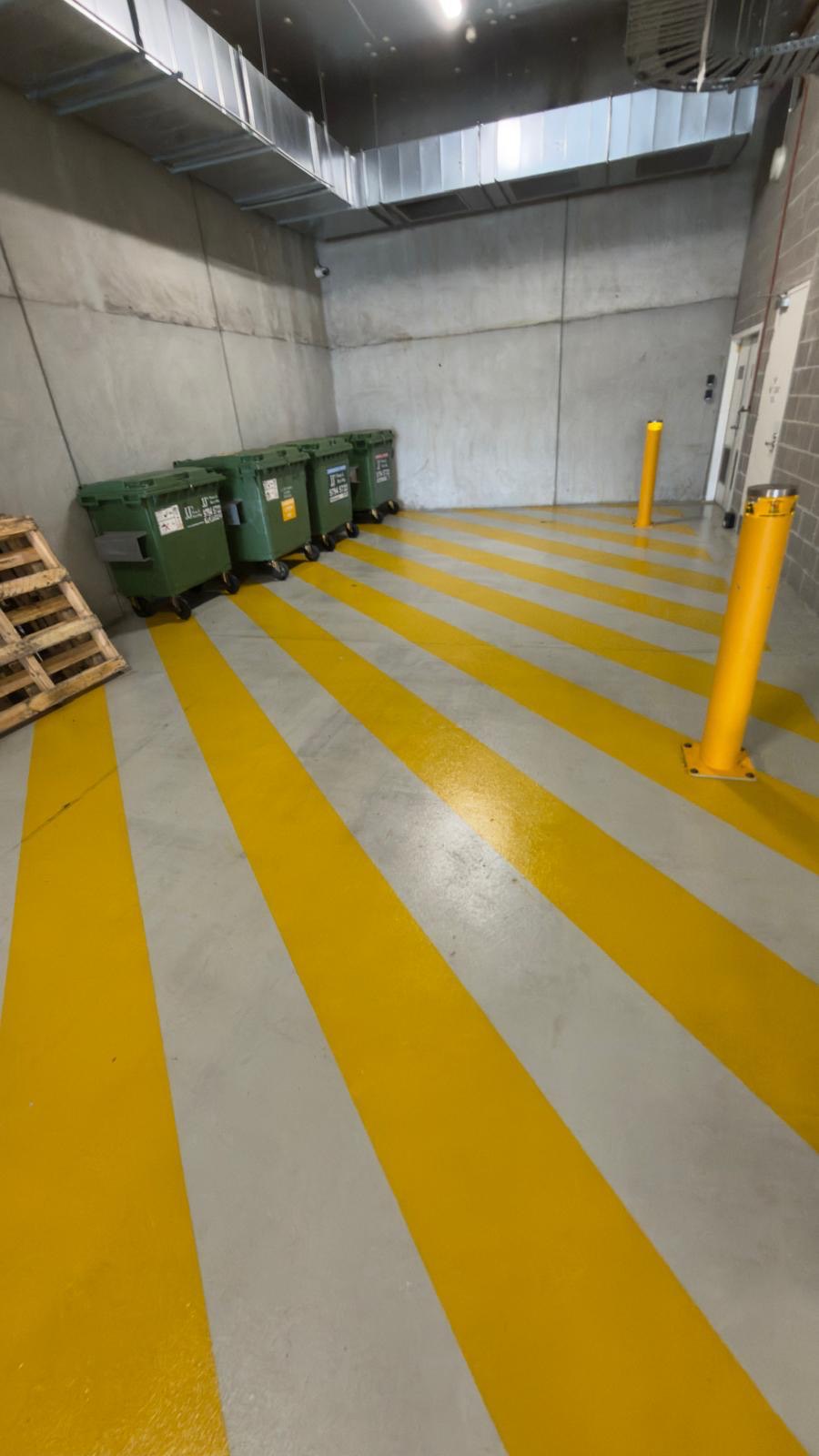 Loading dock bin store floor, dull and marked above, stripped and resealed with crisp yellow safety lines below