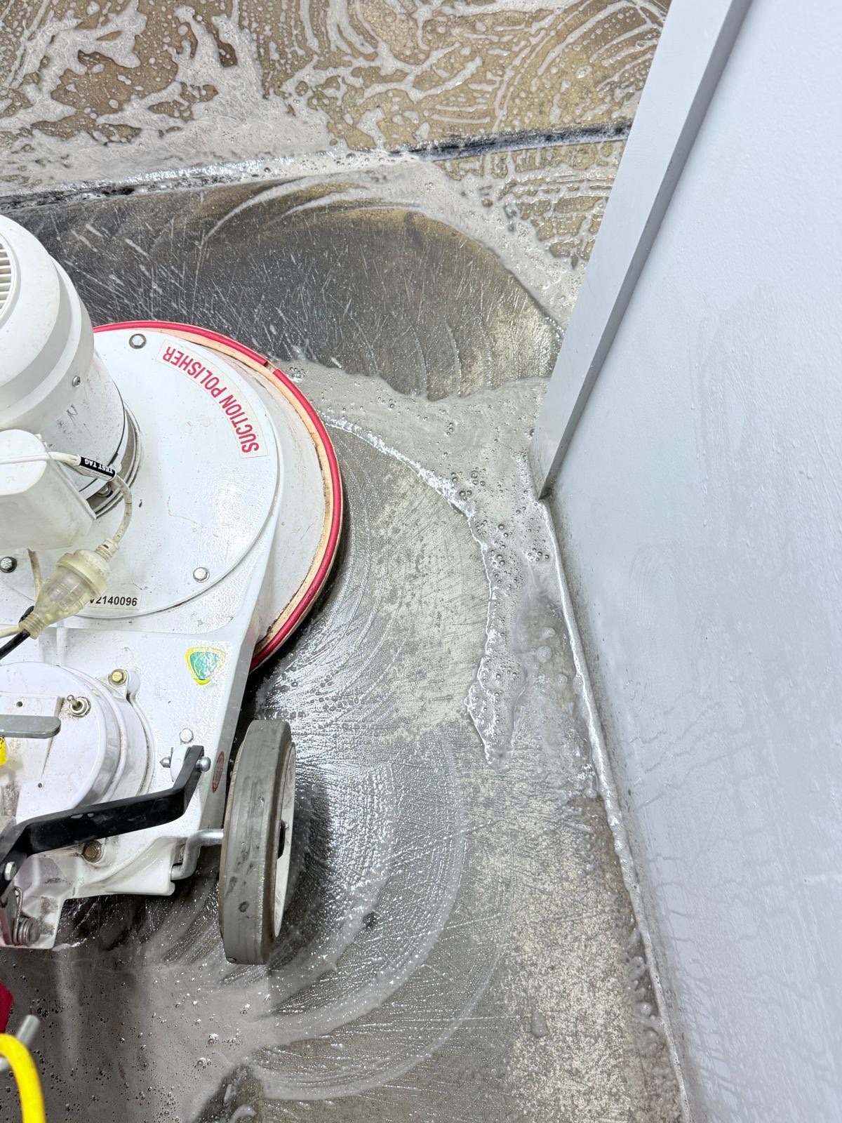 Suction polisher stripping an office hard floor back to bare concrete along the skirting