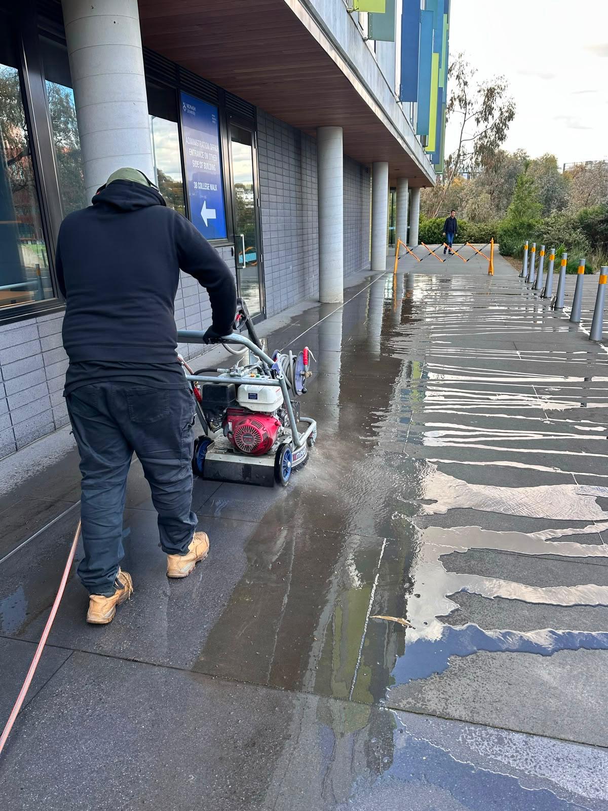 Freshly pressure washed paved walkway beside a school sports field and batting cage